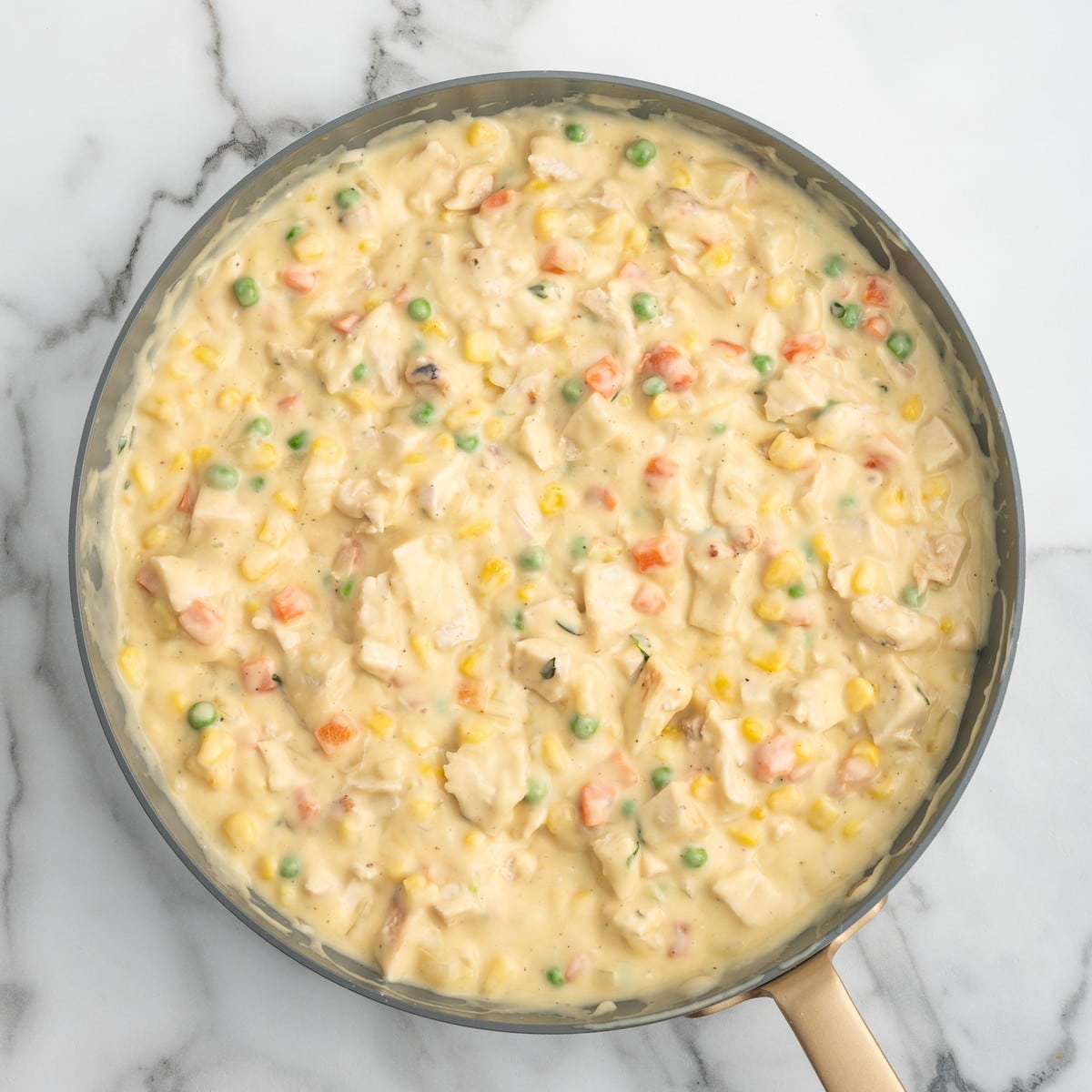 Overhead view of the finished creamy Chicken Pot Pie filling in a skillet with chunks of chicken, peas, carrots, corn, onions, and herbs.