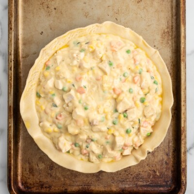 Overhead view of creamy chicken, peas, carrots, and corn filling spooned into the bottom crust of a homemade Chicken Pot Pie.