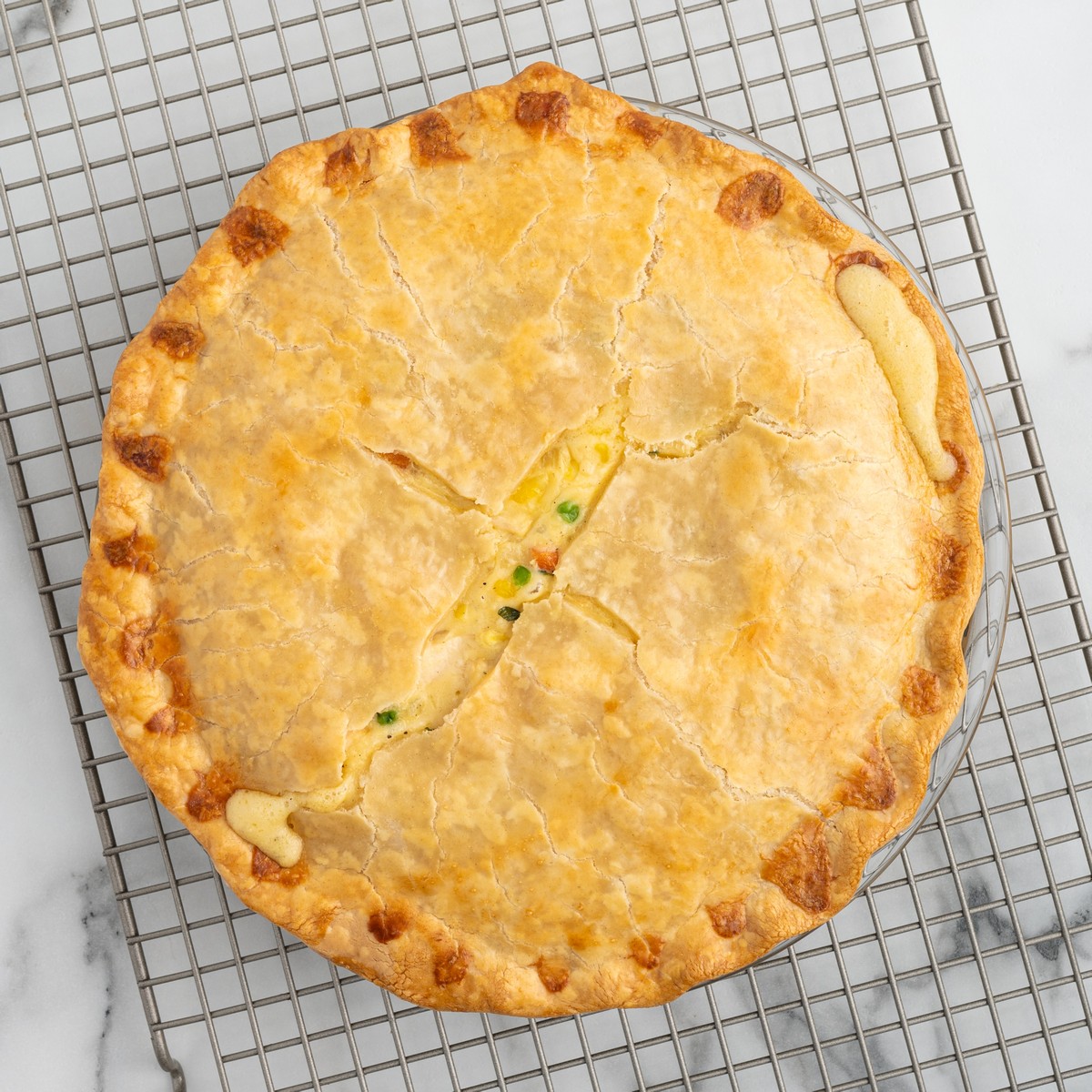 Overhead view of a freshly baked Chicken Pot Pie cooling on a wire rack with a golden double crust and vented center.