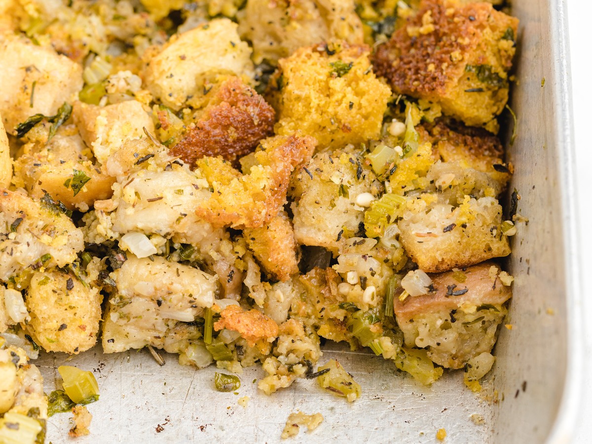 Close-up of homemade Cornbread Stuffing with golden cornbread cubes, bread pieces, celery, onion, and herbs baked together in a roasting pan.