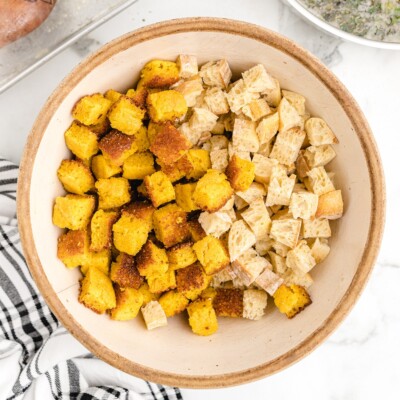 Dried cornbread cubes and dried baguette cubes divided in a large mixing bowl for making homemade Cornbread Stuffing.
