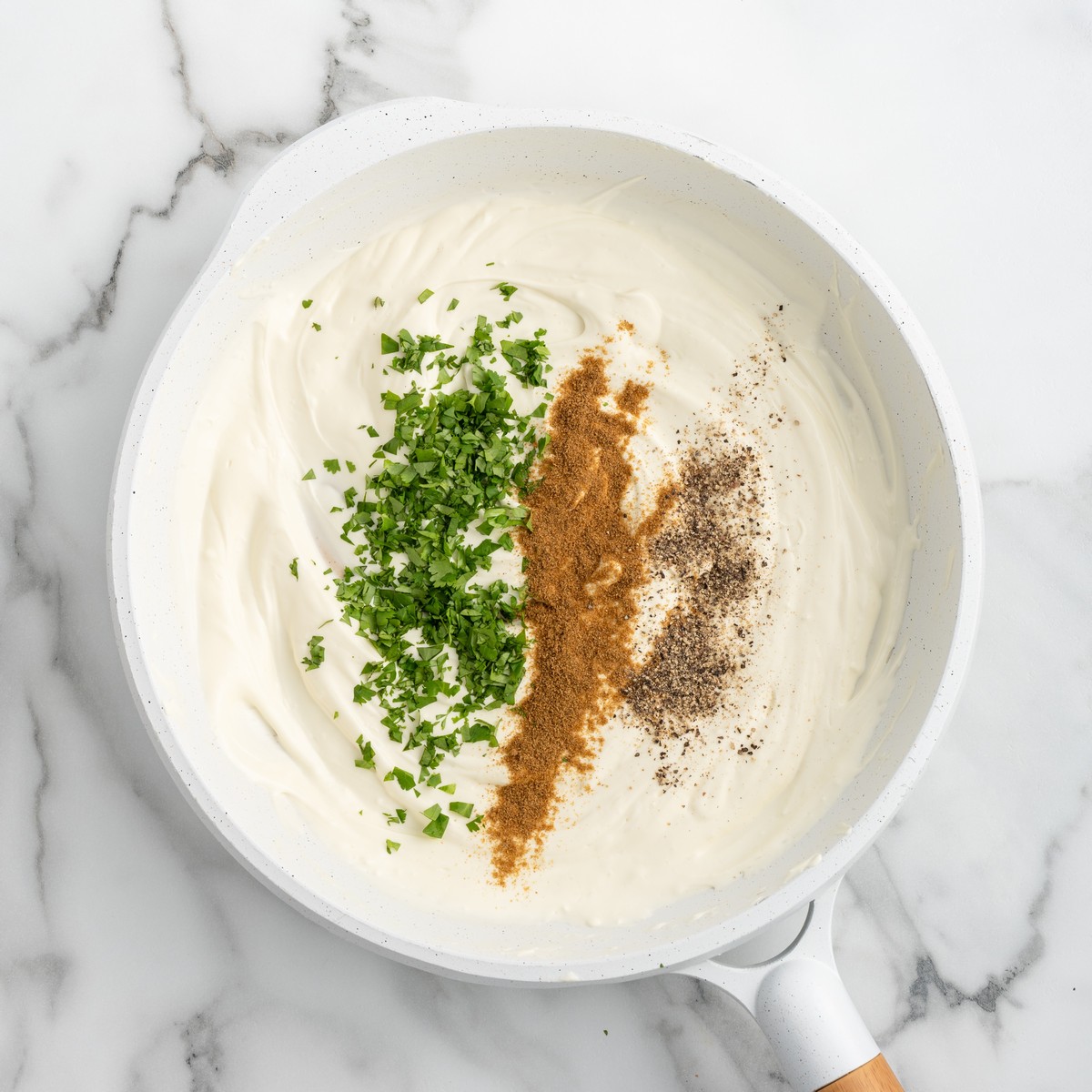 Creamy cream cheese sauce in a skillet topped with chopped cilantro, ground cumin, and black pepper during preparation of Cream Cheese Chicken Enchiladas.