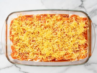 Cream Cheese Chicken Enchiladas arranged in a glass baking dish, covered with red enchilada sauce and a generous layer of shredded Colby Jack cheese before baking.
