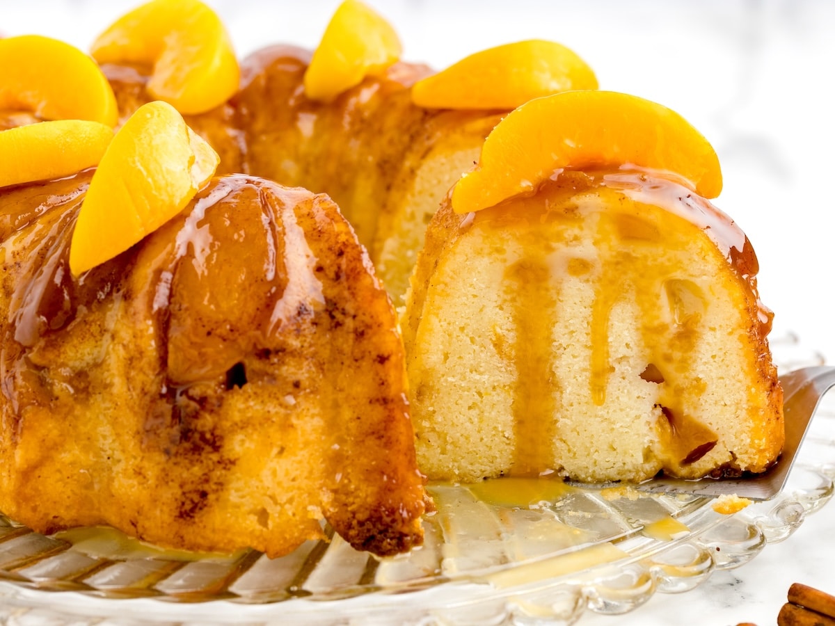 Sliced peach cobbler pound cake showing chopped peaches through the crumb, with caramel and peach slices on top