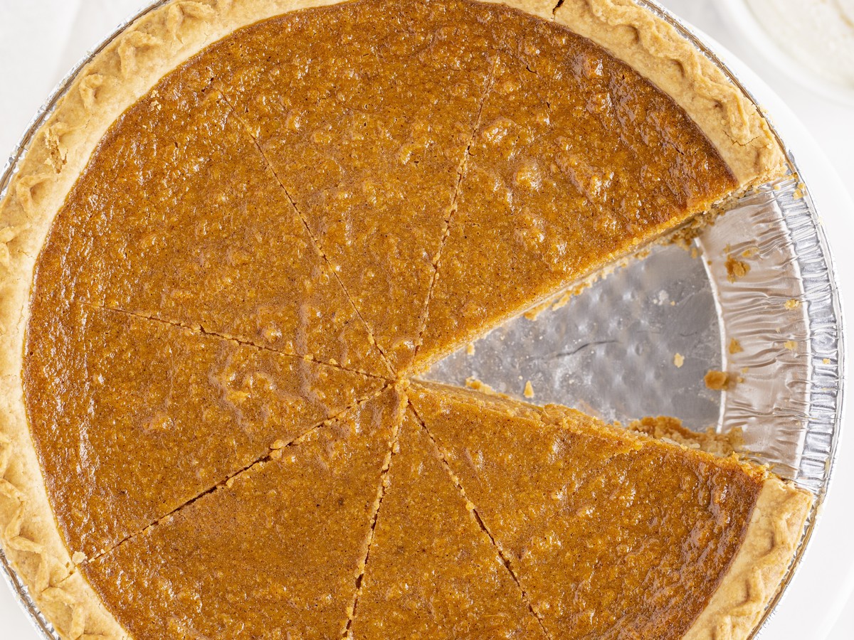Overhead view of a baked Sweet Potato Pie cut into slices, with one wedge removed to reveal the smooth spiced filling and golden crust.