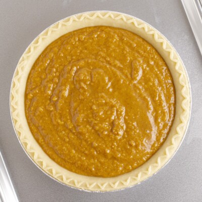 Unbaked Sweet Potato Pie filled with a smooth, spiced sweet potato mixture in a crimped deep-dish pie crust on a baking sheet.