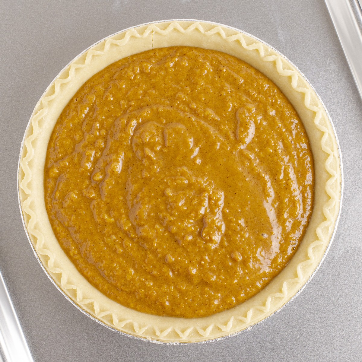 Unbaked Sweet Potato Pie filled with a smooth, spiced sweet potato mixture in a crimped deep-dish pie crust on a baking sheet.