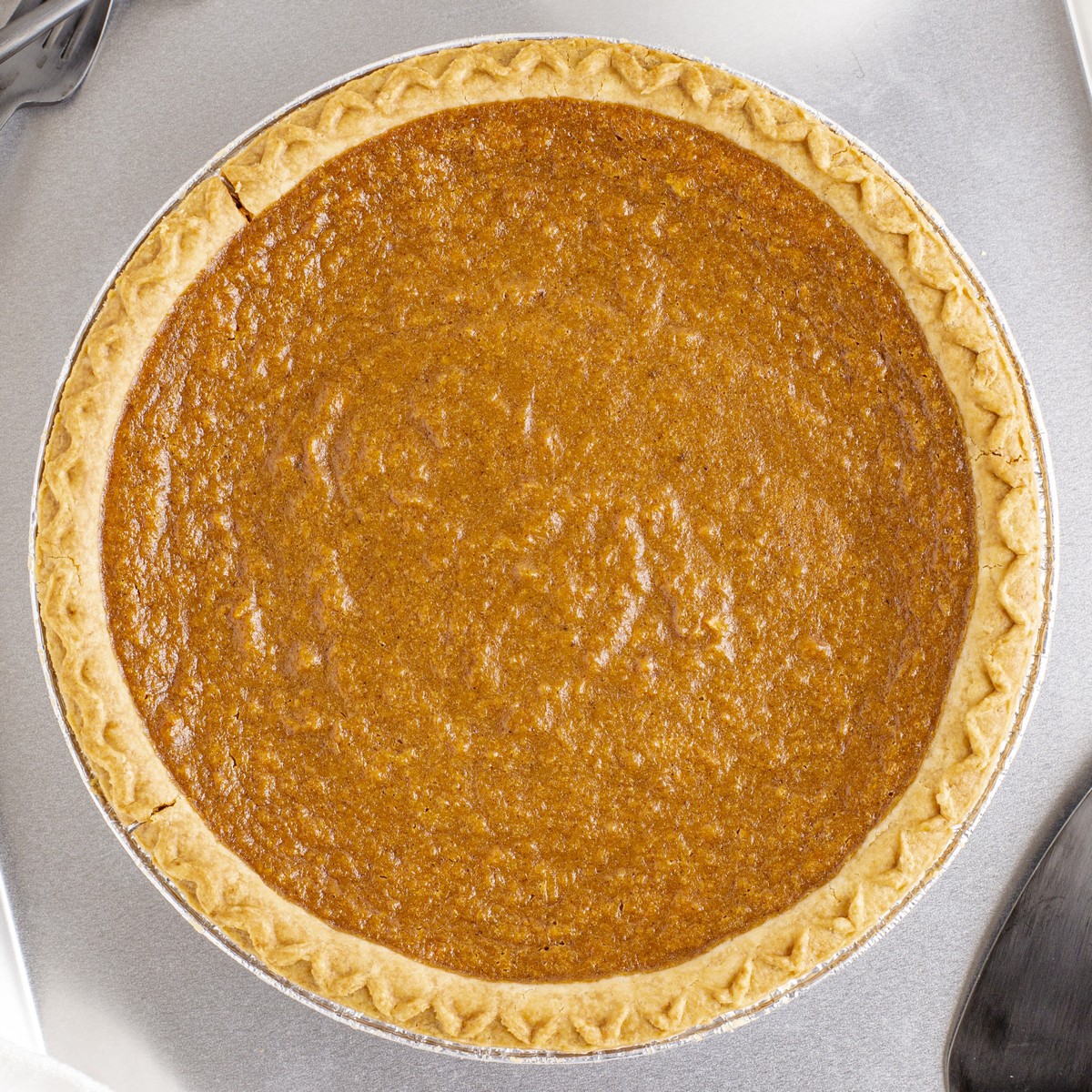 Overhead view of a fully baked Sweet Potato Pie with golden-brown filling and a crimped crust in a disposable pie pan.